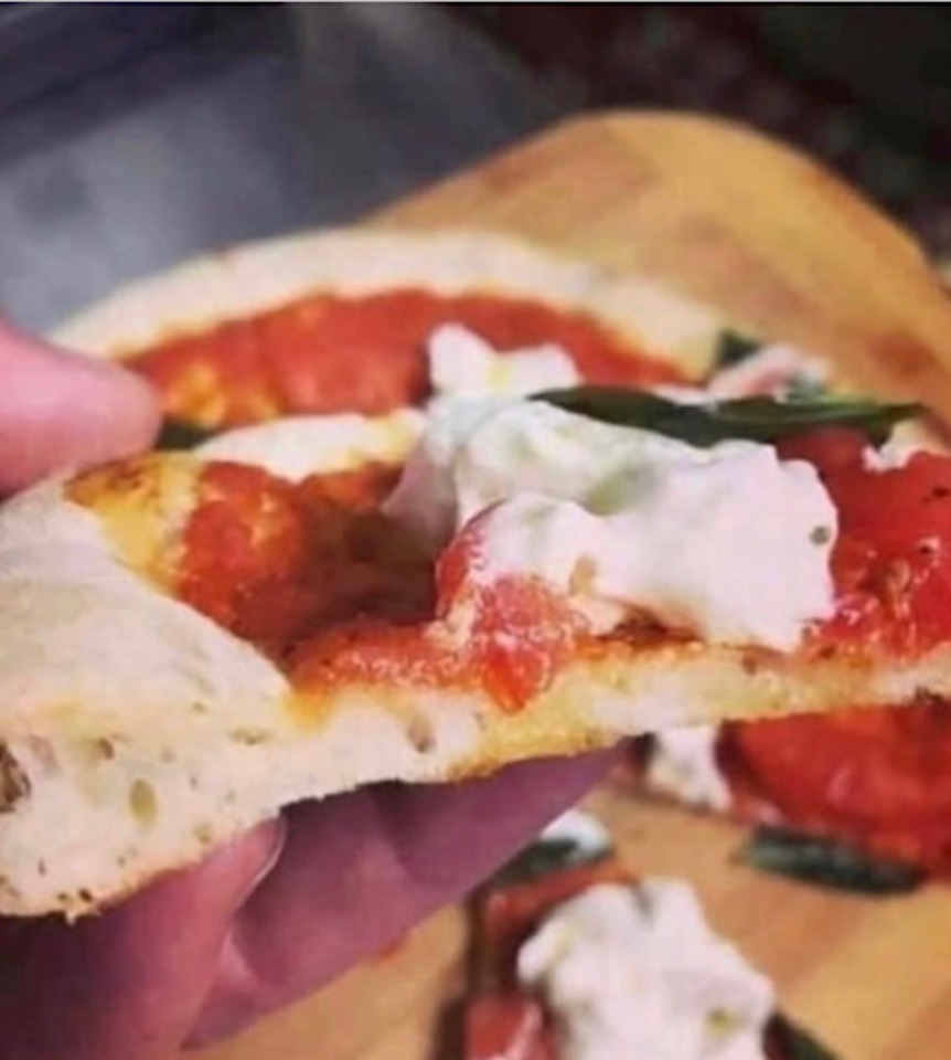 Close up of a slice of pizza with the rest of the pizza out of focus on a wooden board