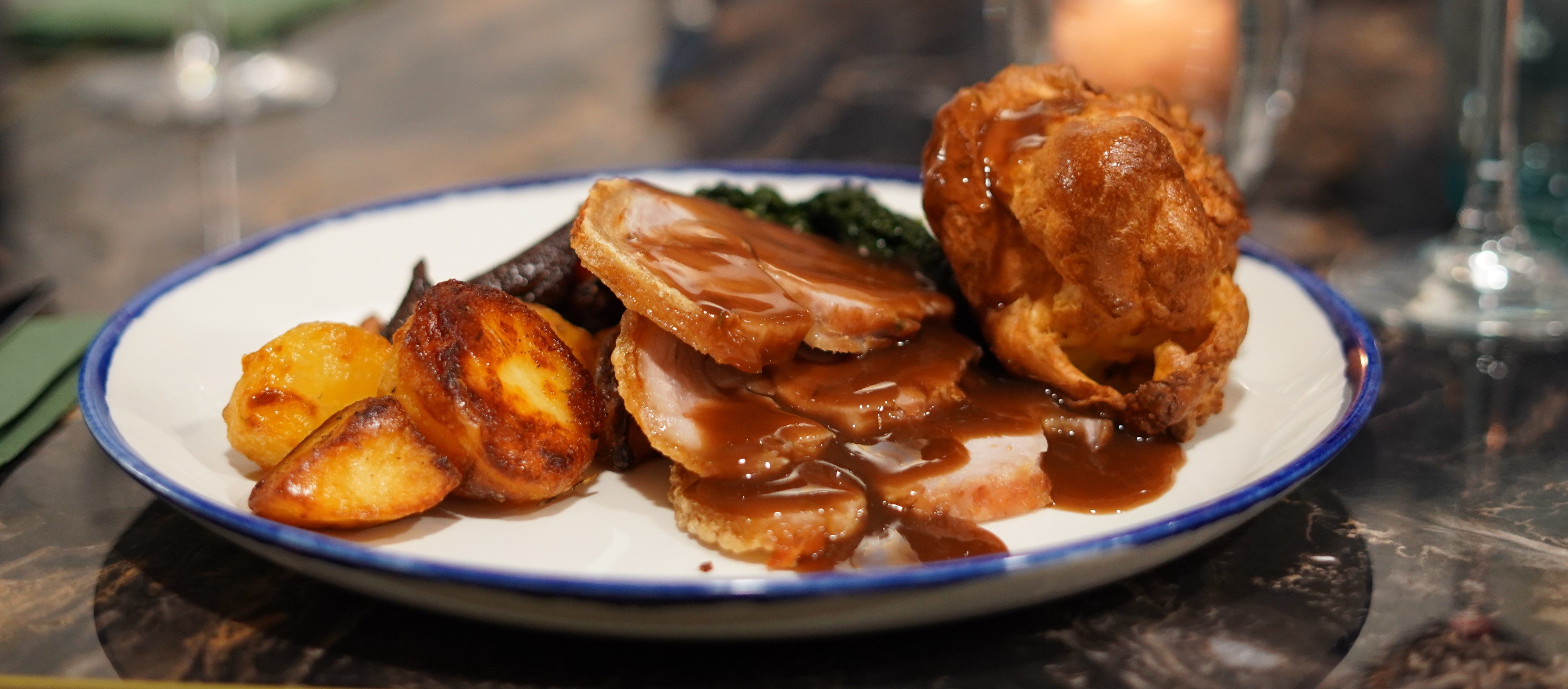 Close up of a roast dinner with gravy and a wine glass out of focus in the background.